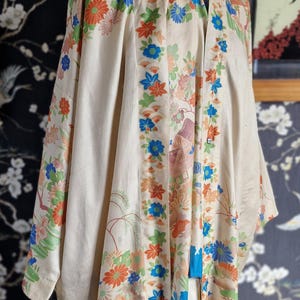 May include: Cream-colored kimono with a floral pattern in orange, blue, and green. The garment features a mandarin collar and long sleeves. The design includes stylized flowers and landscape elements.