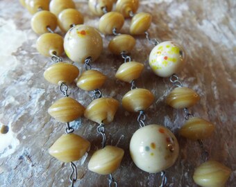 May include: A multi-strand necklace with alternating round and flat beads. The round beads are white with yellow and orange speckles. The flat beads are a light brown colour.