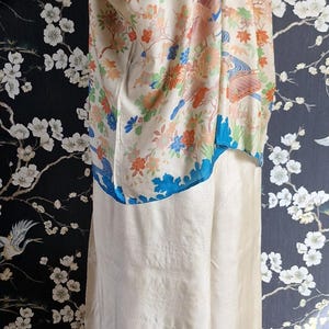May include: Cream-colored vintage kimono with floral and bird pattern. The kimono features a blue trim and is displayed on a mannequin. The background has a floral design. A unique piece of vintage apparel.