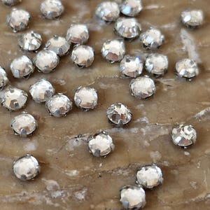 Peut inclure: Une dispersion de strass en verre transparent ton argent avec une finition facetée. Les strass ont un sertissage à griffes.