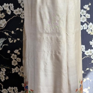 May include: Cream-colored, vintage-style pants with a floral border in shades of blue, orange, and red. The pants are displayed on a mannequin, showcasing the design and fit. The bottom hem is a vibrant blue.