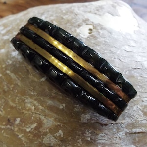 May include: A black and gold hair clip with a textured design. The clip has three gold bands.
