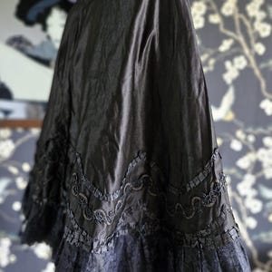 May include: A black satin cape with a lace trim and a ruffled collar. The cape is on a dress form.
