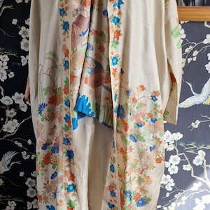 May include: Cream-colored vintage kimono set with a floral pattern in orange, blue, and green. The set includes a long robe and matching pants. The kimono is displayed on a mannequin.