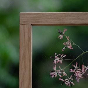 Pode incluir: Uma moldura de madeira com um painel de vidro transparente, mostrando um ramo delicado de flores cor-de-rosa com caules escuros. As flores s&atilde;o prensadas e preservadas dentro da moldura, criando uma obra de arte bot&acirc;nica.
