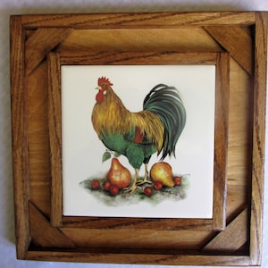 May include: A wooden frame with a tile insert featuring a colorful rooster with a green, yellow, and red plumage standing on a white background with pears and red berries.