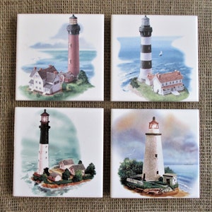 May include: Set of four ceramic tile coasters featuring watercolor paintings of lighthouses. Each coaster depicts a different lighthouse with a white background and blue water.