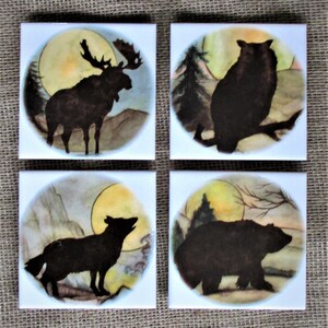 May include: Set of four ceramic coasters featuring silhouettes of a moose, owl, fox, and bear against a watercolor background with a full moon.
