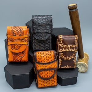 May include: Five leather cigarette cases with intricate designs. Two are brown with floral patterns, one is black with a woven pattern, and two are orange with a woven pattern.