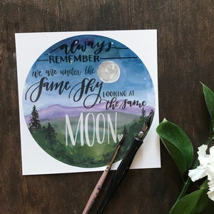 May include: A watercolor painting of a night sky with a full moon and a quote that reads "always remember we are under the same sky looking at the same moon".
