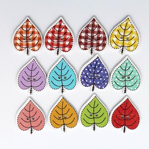 May include: Twelve wooden leaf-shaped buttons with various patterns. The buttons are in shades of red, yellow, blue, green, and purple. Some buttons have a checkered pattern, while others have polka dots.