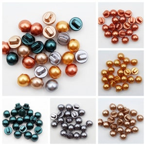 May include: Assortment of pearl-like buttons in various colours, including gold, silver, green, and copper. The buttons have a flat back and a raised dome shape.
