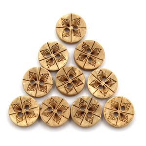 May include: A collection of ten round, light-colored wooden buttons arranged in a triangular shape. Each button features a four-petal floral design etched in a darker brown color, with four holes for sewing.
