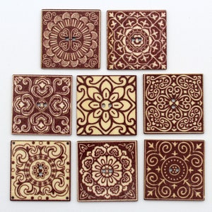 May include: Seven square wooden buttons with intricate, symmetrical patterns in shades of brown and beige. Each button features a different design, including floral and geometric motifs, and has two holes for sewing.