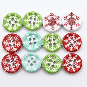 May include: A collection of twelve round wooden buttons with snowflake designs. The buttons are in various colors, including green, red, white, and light blue. Each button has four holes for sewing.