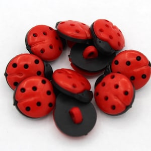 May include: A group of red and black ladybug buttons with black dots and a black back. The buttons have a raised design and are made of plastic.