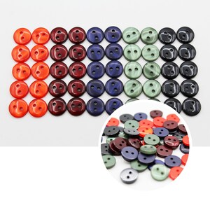 May include: Assortment of colourful plastic buttons in red, orange, green, blue, and black. The buttons are arranged in rows and columns.
