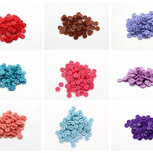 May include: Assortment of two-hole plastic buttons in various colours, including red, brown, purple, blue, pink, and light blue. The buttons are arranged in piles on a white background.
