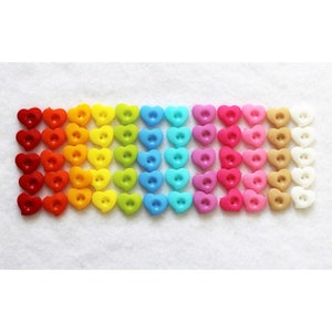 May include: A rainbow assortment of heart-shaped buttons in various colors, including red, orange, yellow, green, blue, purple, pink, beige, and white.