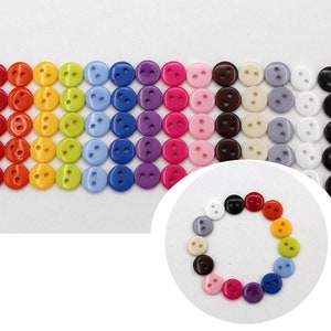 May include: Assortment of colourful plastic buttons in various shades of red, orange, yellow, green, blue, purple, pink, brown, white, and black. The buttons are arranged in rows, with each row featuring a different colour.