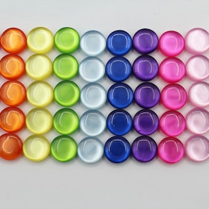 Peut inclure: Une collection de 48 perles rondes en verre de style cabochon dans un arc-en-ciel de couleurs. Les perles sont disposées en rangées, passant du rouge à l'orange, au jaune, au vert, au bleu, au violet, au rose et au blanc. Chaque perle a une surface lisse et brillante.