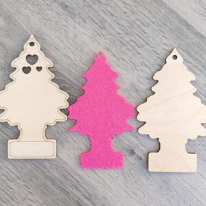 Puede incluir: Tres adornos de &aacute;rbol de Navidad. Dos son de madera clara, uno con recortes de coraz&oacute;n. El tercero es un &aacute;rbol de fieltro rosa vibrante. Todos tienen un agujero en la parte superior para colgar y una base rectangular.