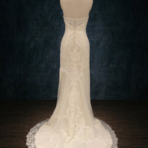 May include: A white strapless wedding dress with a lace overlay and a long train. The dress is fitted and has a sweetheart neckline. The back of the dress features a zipper closure and a row of buttons.