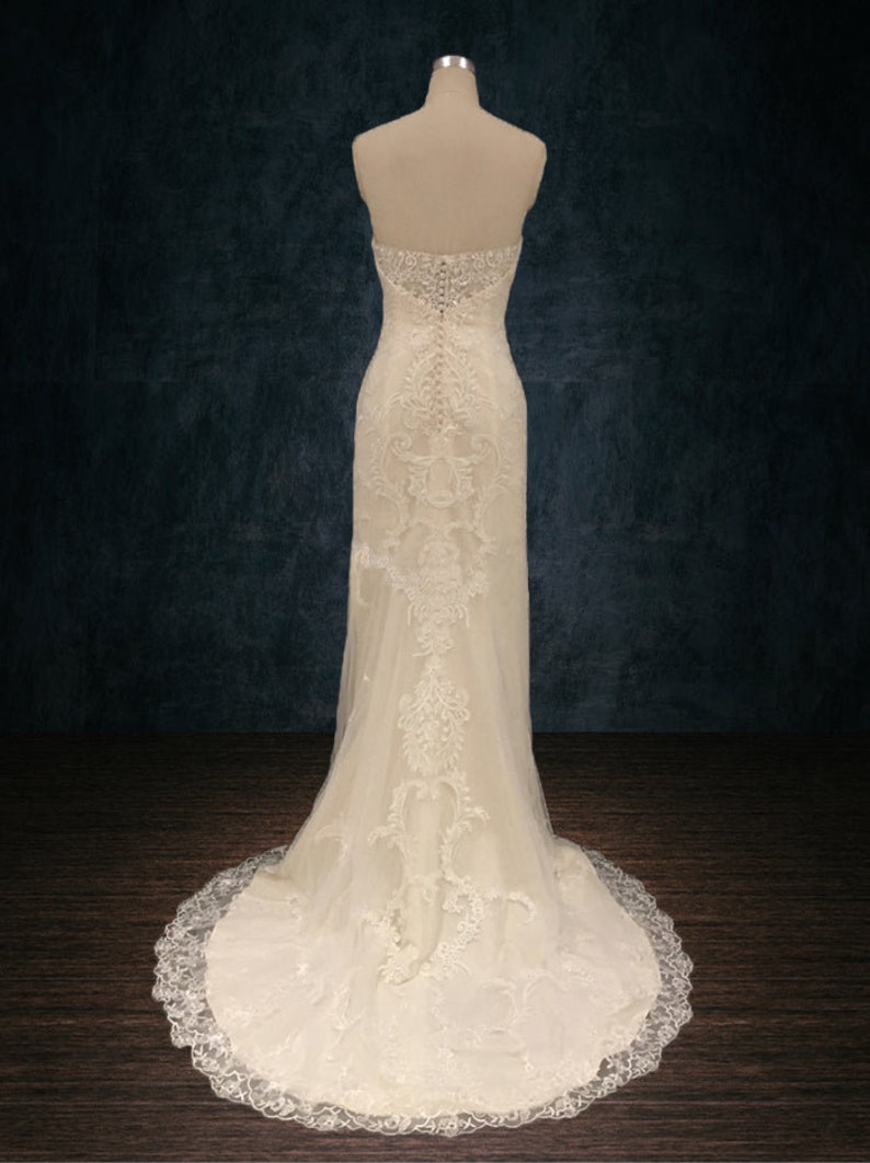 May include: A white strapless wedding dress with a lace overlay and a long train. The dress is fitted and has a sweetheart neckline. The back of the dress features a zipper closure and a row of buttons.