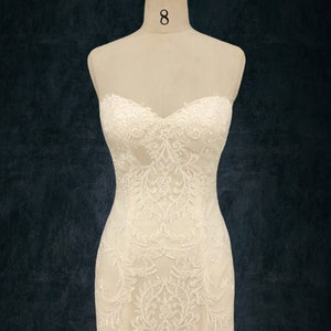 May include: A white strapless wedding dress with intricate lace detailing. The dress has a fitted bodice and a flowing skirt.