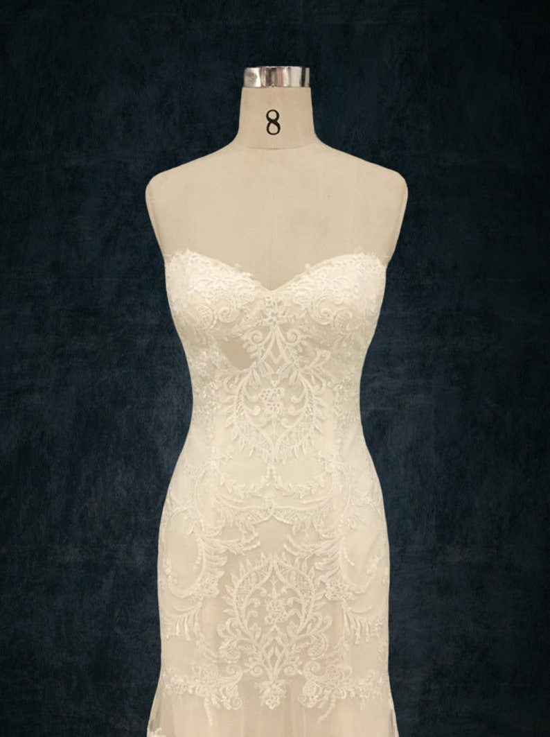 May include: A white strapless wedding dress with intricate lace detailing. The dress has a fitted bodice and a flowing skirt.