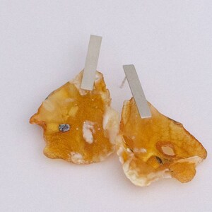 Könnte beinhalten: Ein Paar Bernstein-Ohrringe mit silbernen Balkenakzenten. Der Bernstein ist ein natürliches, organisches Material mit einer warmen, honigartigen Farbe. Die Ohrringe sind ein einzigartiges und stilvolles Schmuckstück.