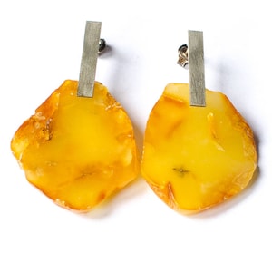 Könnte beinhalten: Ein Paar Bernstein-Ohrringe mit silbernen Stäben. Der Bernstein ist hellgelb und hat eine natürliche, unregelmäßige Form.