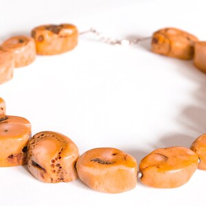 May include: A necklace made of natural coral beads. The beads are a light orange color and have a rough, textured surface. The necklace is strung on a silver chain.