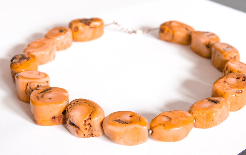 May include: A necklace made of natural coral beads. The beads are a light orange color and have a rough, textured surface. The necklace is strung on a silver chain.