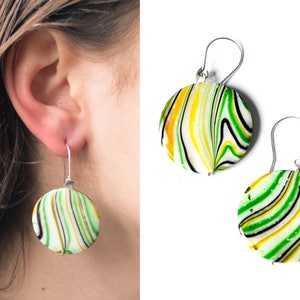 Könnte beinhalten: Ein Paar grüne, gelbe und schwarze marmorierte Kreisohrringe mit silbernen Haken.