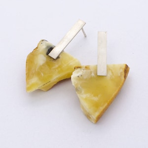 Könnte beinhalten: Ein Paar Bernstein-Ohrringe mit silbernen Stiften. Der Bernstein ist hellgelb und hat eine natürliche, unregelmäßige Form.