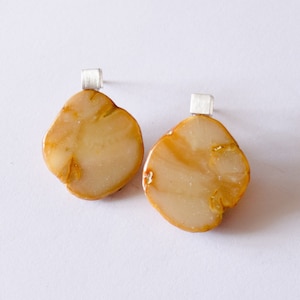 Könnte beinhalten: Ein Paar Ohrringe mit einer einzigartigen, organischen Form. Die Ohrringe sind aus einem hellbraunen Material mit einem marmorierten Muster und haben silberne Ohrstecker.
