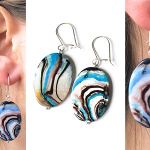 Könnte beinhalten: Ein Paar silberne Ohrhänger mit ovalen, marmorierten Steinen aus blauer, weißer und brauner Harz.