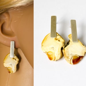 Könnte beinhalten: Ein Paar Bernstein-Ohrringe mit silbernen Stäben, die daran hängen. Der Bernstein ist hellgelb mit braunen Streifen.