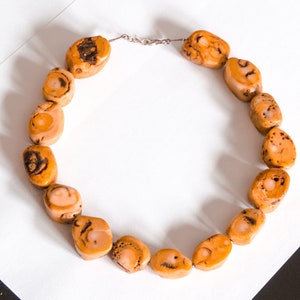 May include: A necklace made of natural brown and beige stone beads. The beads are irregularly shaped and have a mottled pattern.