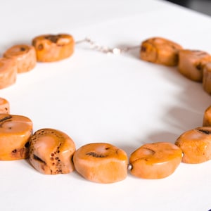 May include: A necklace made of light orange coral beads. The beads are oval shaped and have a natural, textured surface.