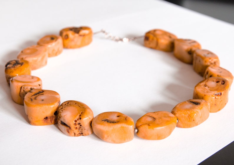 May include: A necklace made of light orange coral beads. The beads are oval shaped and have a natural, textured surface.