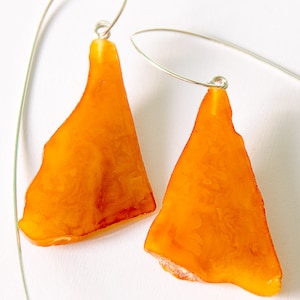 May include: A pair of amber earrings with silver hooks. The amber is a warm orange color and has a natural, irregular shape.