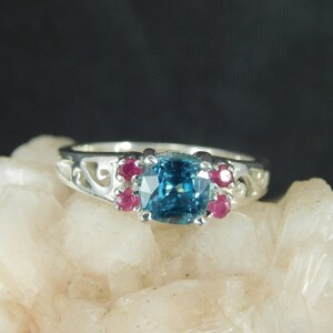 May include: A silver ring with a blue gemstone surrounded by four smaller pink gemstones.