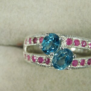 May include: A silver ring with two blue topaz gemstones and a row of pink ruby stones around the band.