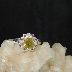 May include: A silver ring with a large yellow gemstone surrounded by smaller red gemstones.