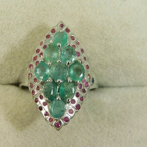 May include: A silver ring with a teardrop-shaped setting featuring a cluster of green emeralds surrounded by smaller pink rubies.