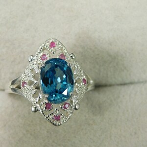 May include: A silver ring with a large blue oval gemstone surrounded by smaller pink gemstones.