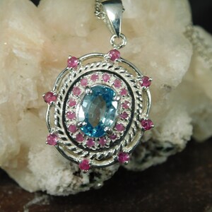 May include: A silver pendant with a blue topaz gemstone surrounded by a halo of pink sapphires.