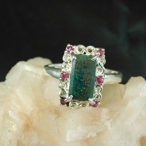 May include: A silver ring with a green opal gemstone set in a filigree design. The ring is accented with small pink gemstones.